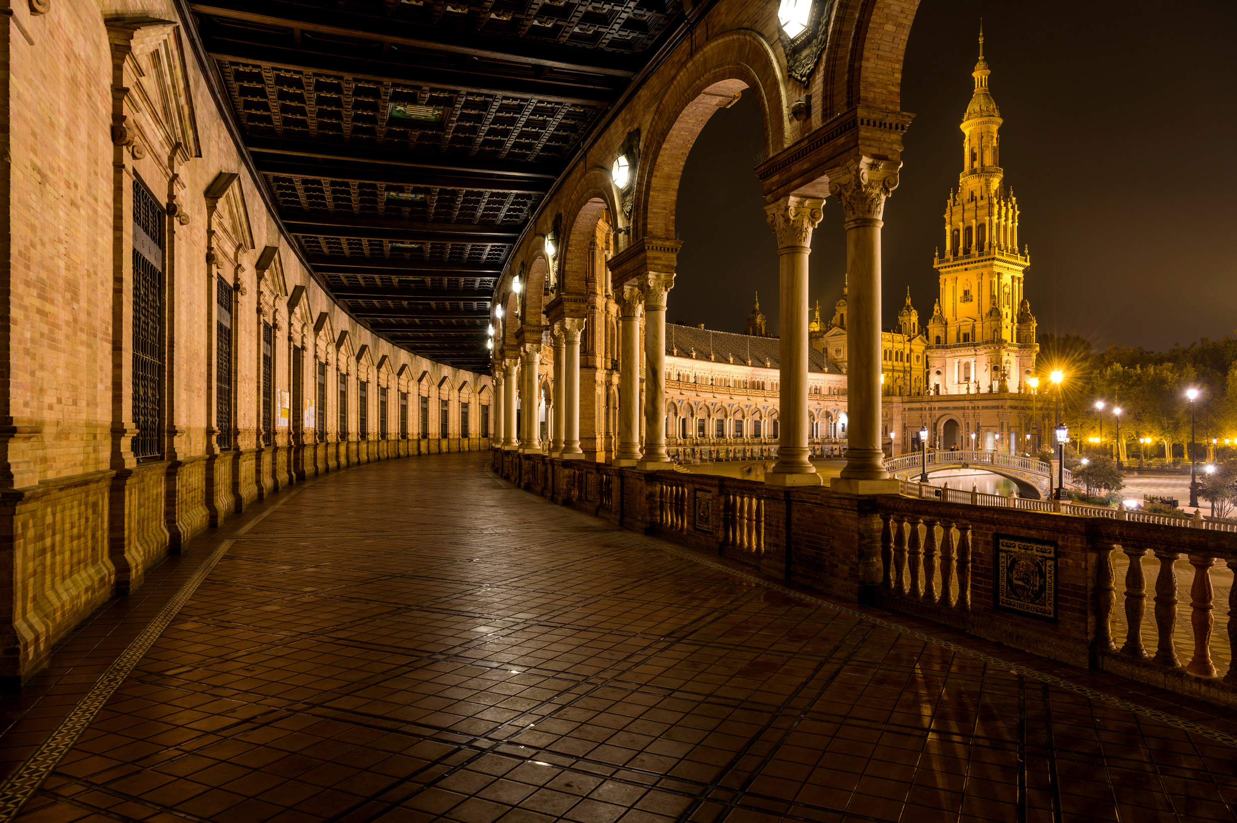 Spanish Square - A wide-angle night view of the illuminated ground-level portico curving along the semi-circular brick building at Spanish Square - Plaza de España, Seville. Andalusia, Spain.